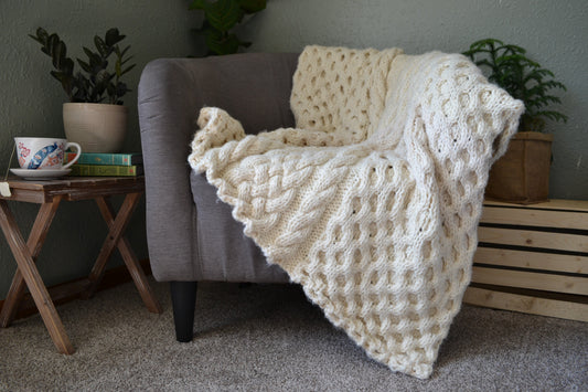 cable knit blanket featuring braided cables vertically up the middle and large sections of honeycomb cables on each side using lion brand thick and quick yarn