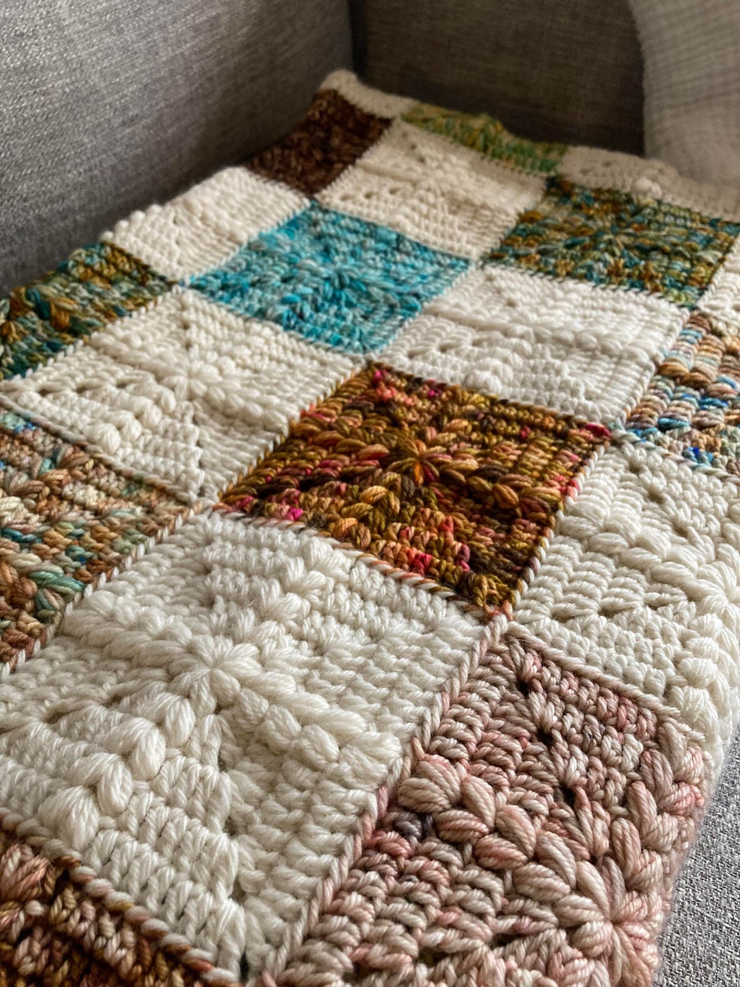 crochet granny squares with a puff stitch cross detail are put together to form a quilt style patchwork blanket