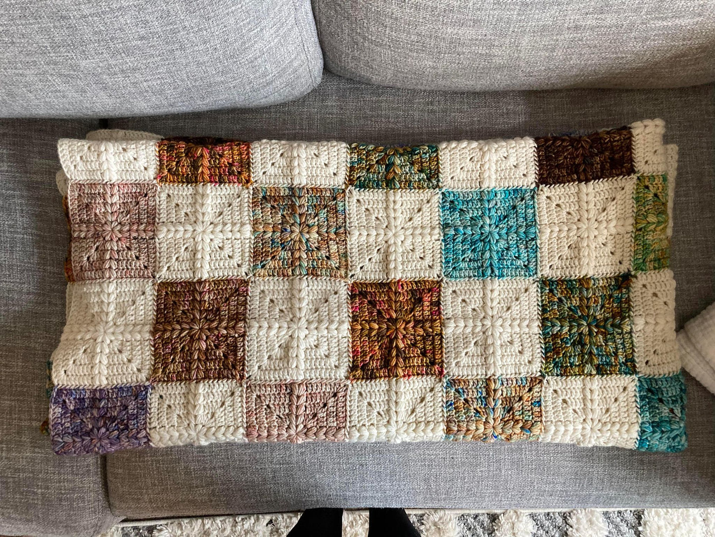 crochet granny squares with a puff stitch cross detail are put together to form a quilt style patchwork blanket