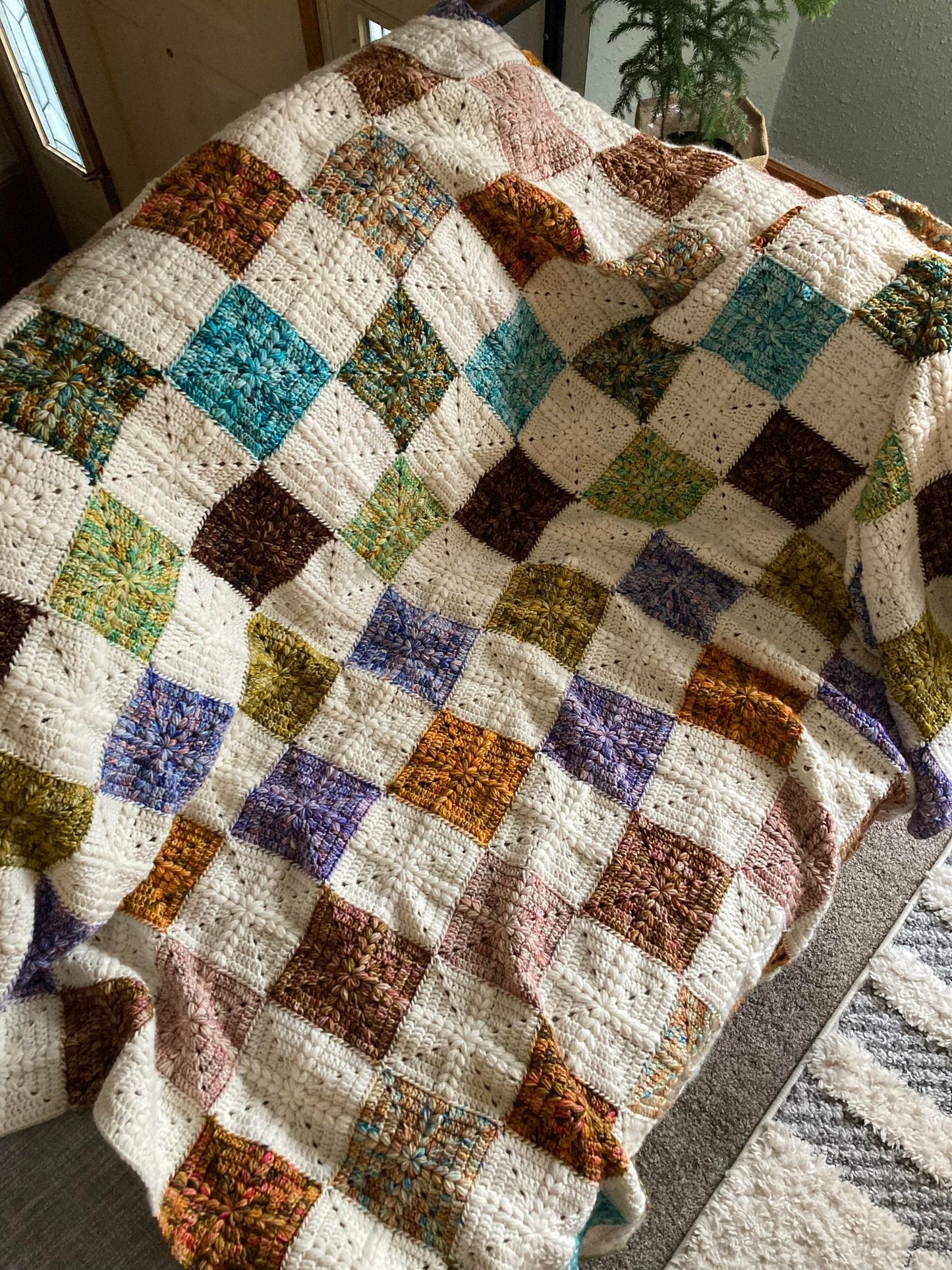 crochet granny squares with a puff stitch cross detail are put together to form a quilt style patchwork blanket