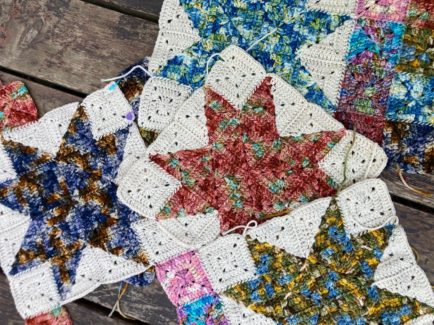 crochet granny squares in solid blocks and in star block are seamed together to create a scrappy crochet quilt