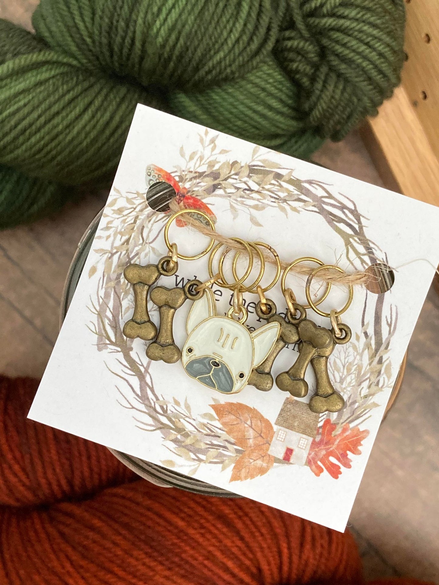 four bronze bone stitch markers paired with a white french bulldog stitch marker