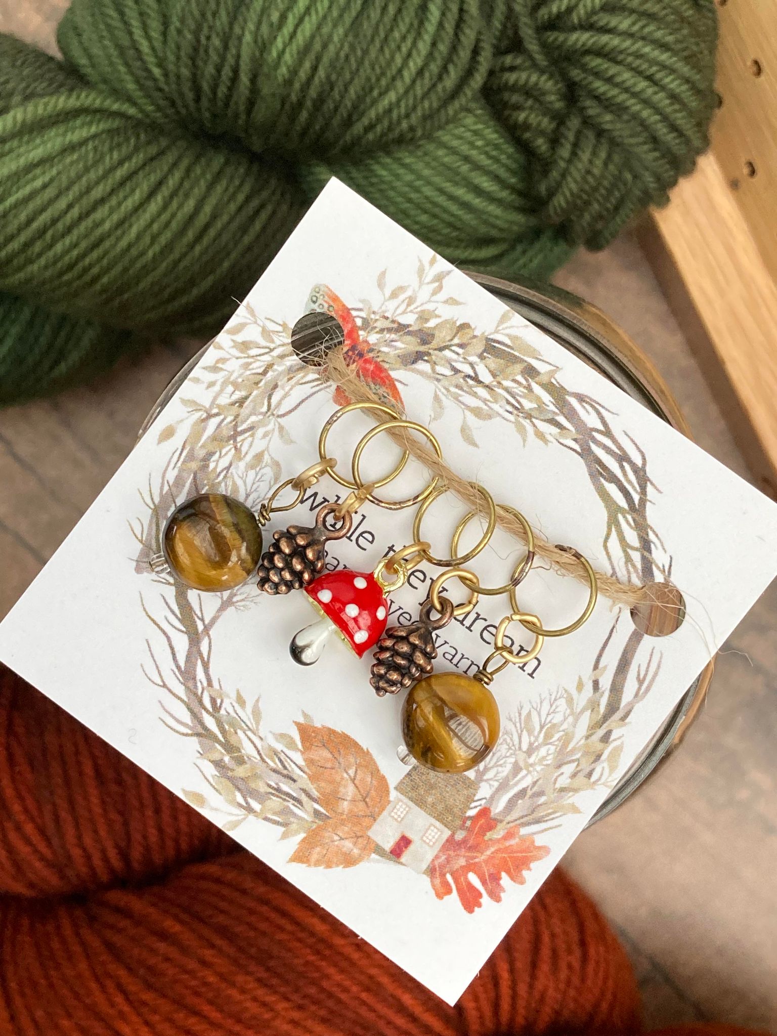 two gemstone stitch markers paired with two bronze pinecone stitch markers and one glass toadstool mushroom stitch marker
