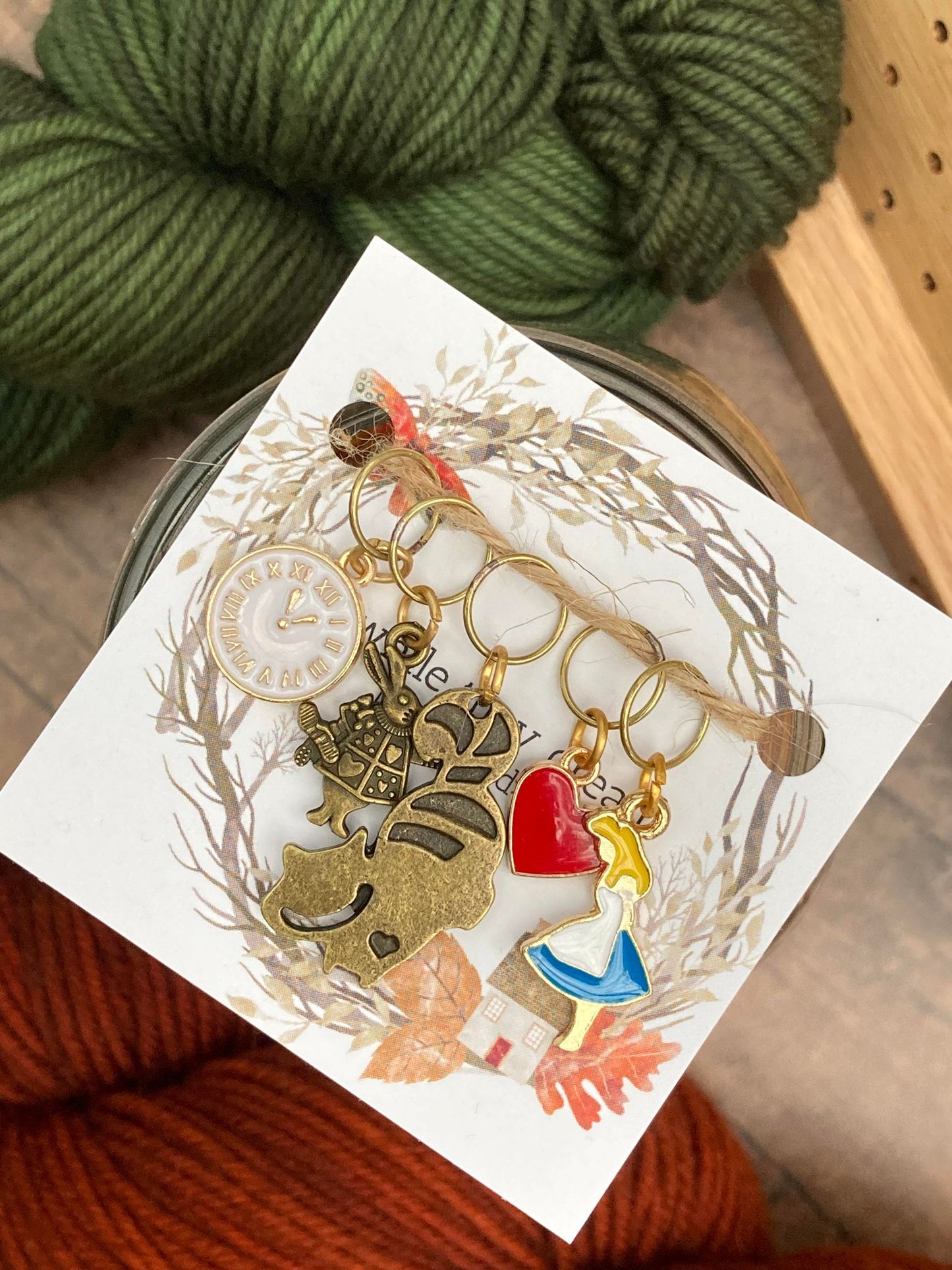White clock stitch marker, white rabbit stitch marker, cheshire cat stitch marker, queen of hearts stitch marker, and alice in wonderland stitch marker