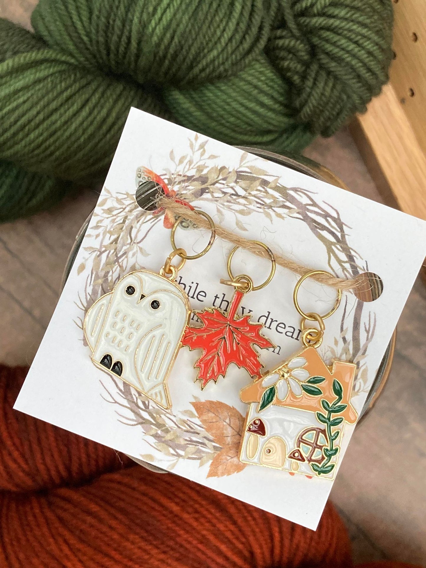 one white owl stitch marker, one orange maple leaf stitch marker, and one cottage with ivy and toadstools stitch marker