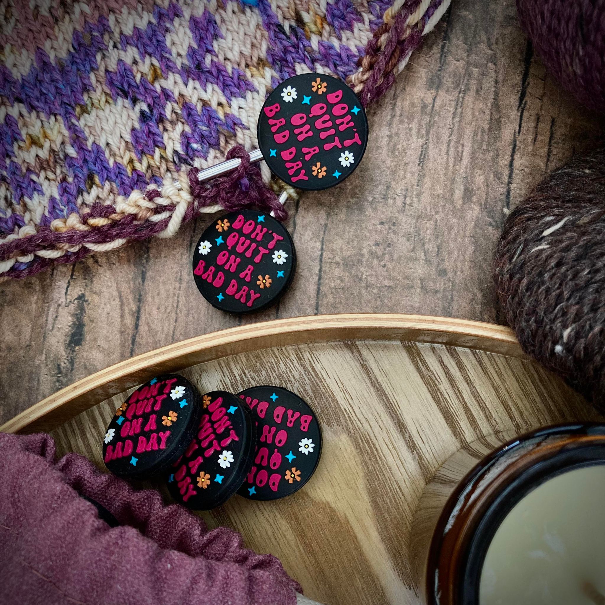 black circular needle stoppers that read "don't quit on a bad day" in pink