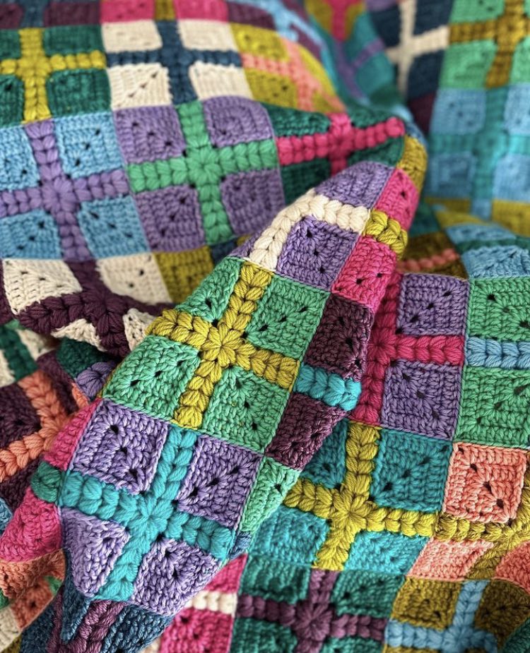 crochet granny squares with a puff stitch cross detail are put together to form a quilt style patchwork blanket