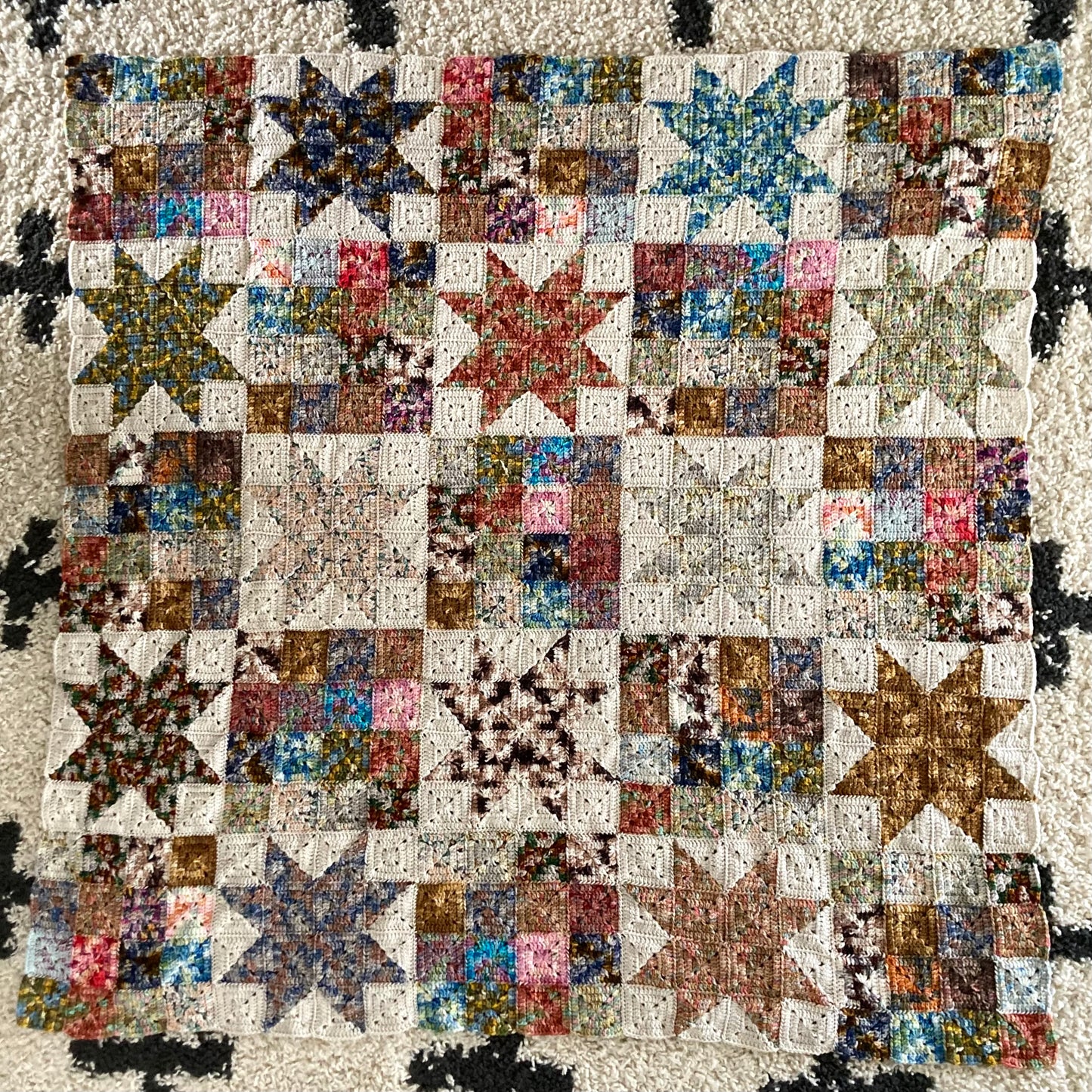 crochet granny squares in solid blocks and in star block are seamed together to create a scrappy crochet quilt