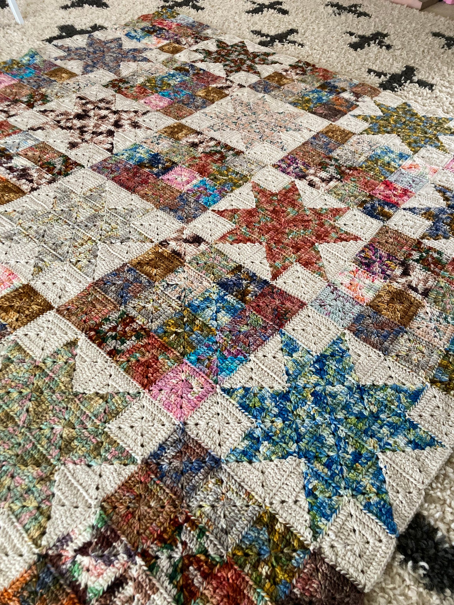 crochet granny squares in solid blocks and in star block are seamed together to create a scrappy crochet quilt