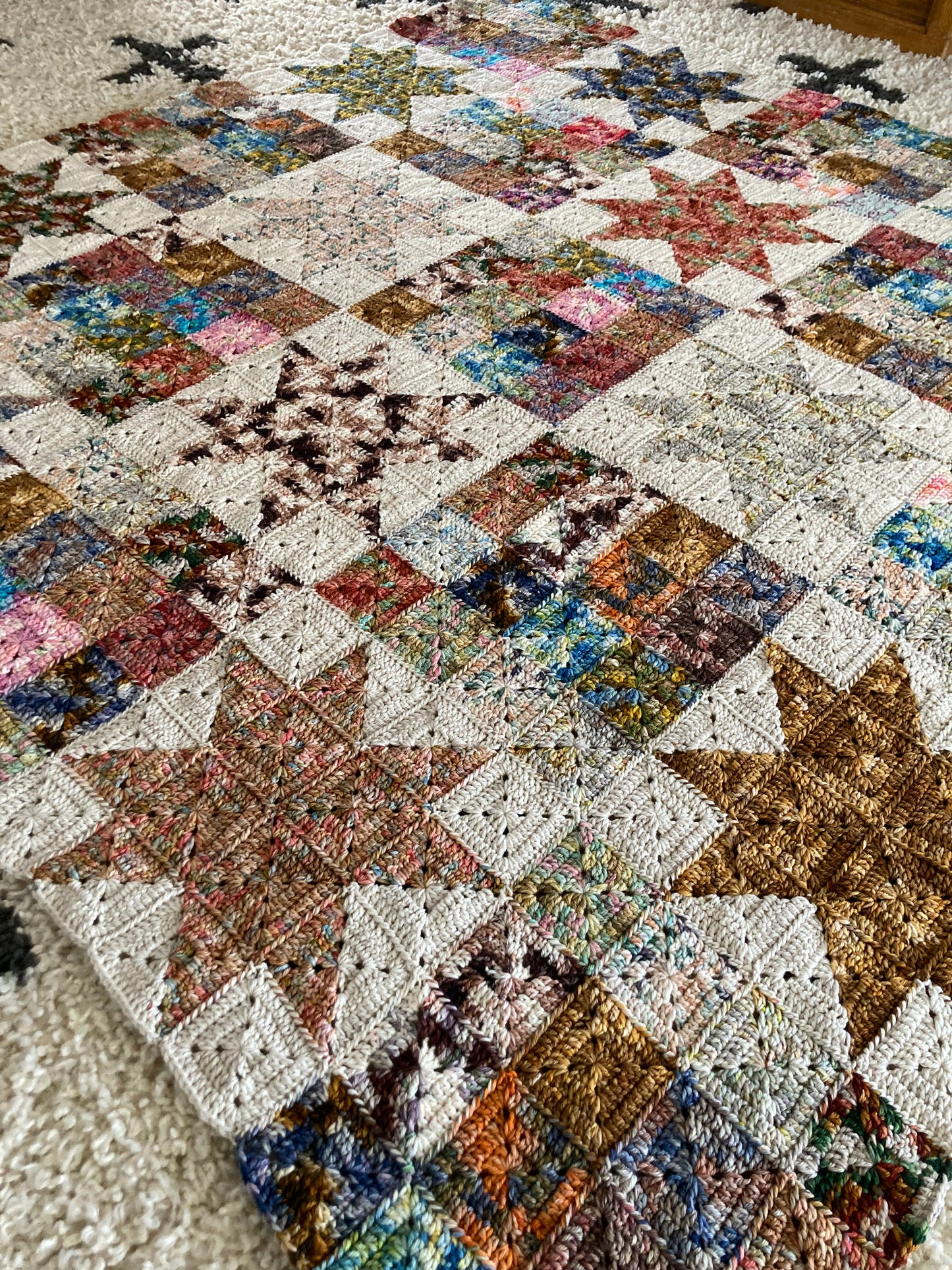 crochet granny squares in solid blocks and in star block are seamed together to create a scrappy crochet quilt