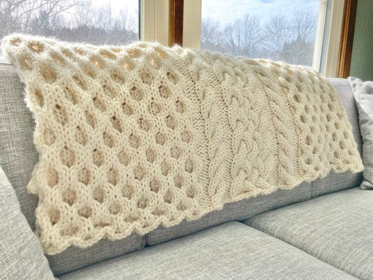 cable knit blanket featuring braided cables vertically up the middle and large sections of honeycomb cables on each side
