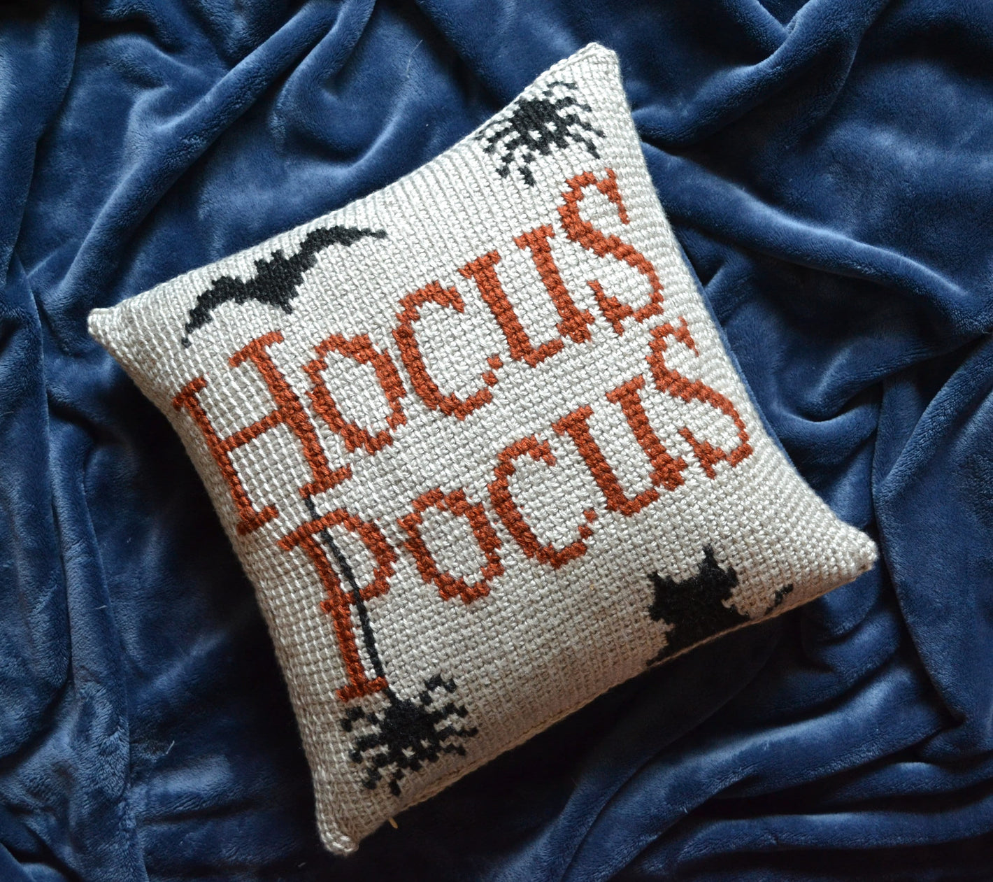 tunisian crochet pillow cover featuring "hocus pocus" crocheted across it, with two spiders, a bat, and a cat